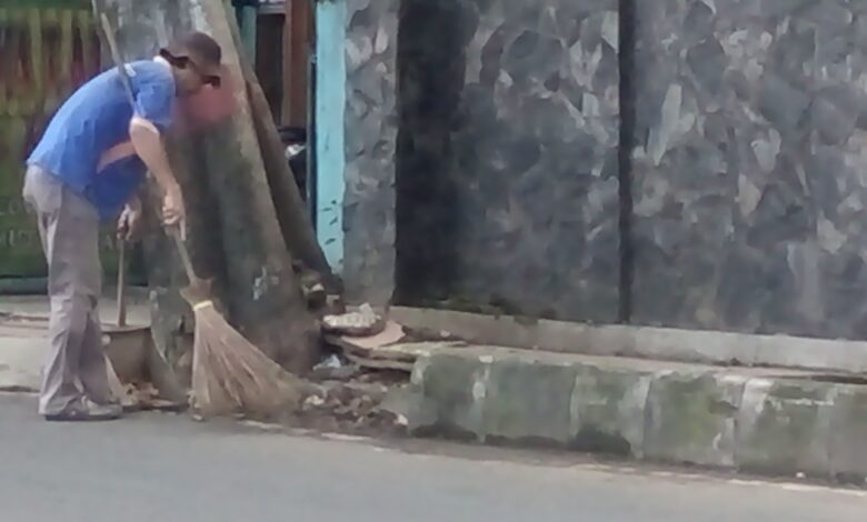 Seorang petugas sedang menyapu jalan agar terlihat bersih.