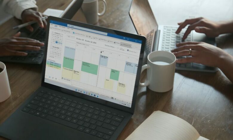 Three people in a meeting at a table discussing schedule on their Microsoft laptop