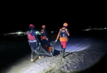 Petugas tim SAR gabungan menggotong kantong jenazah saat melakukan penyisiran dan evakuasi di area pantai pada malam hari.